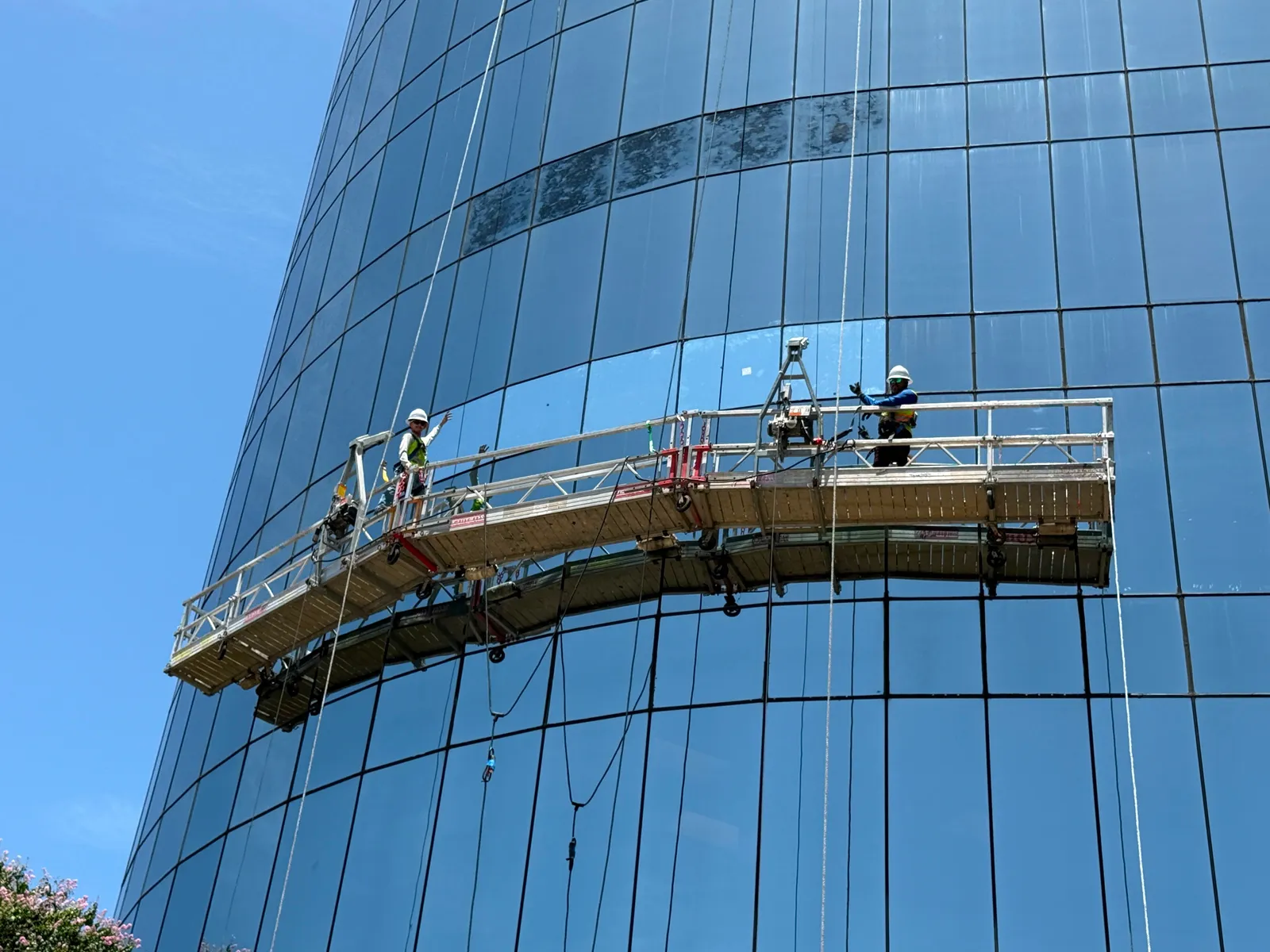 Glaziers installing curved facade glass on suspended platform — Tell Projects Houston
